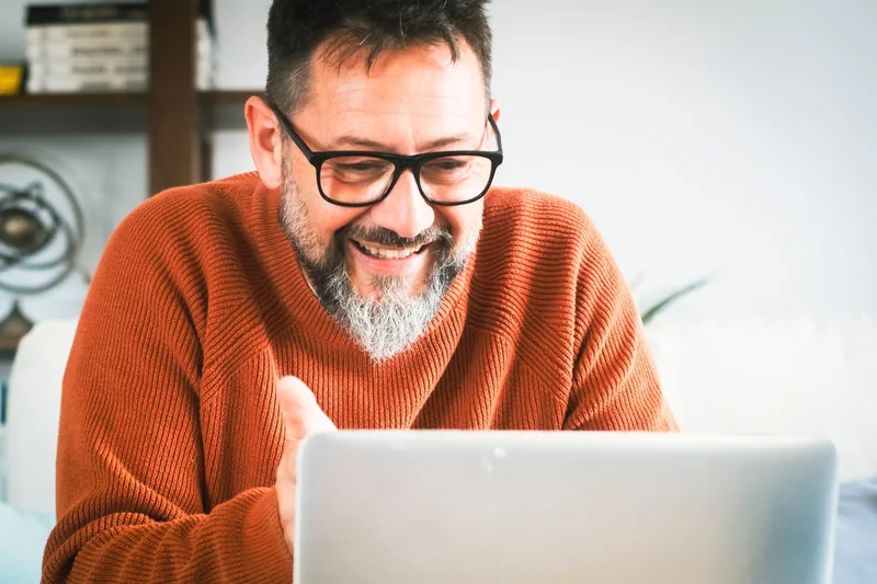 Man die glimlachend naar zijn laptop kijkt, met de rust van een geregeld verkoopproces
